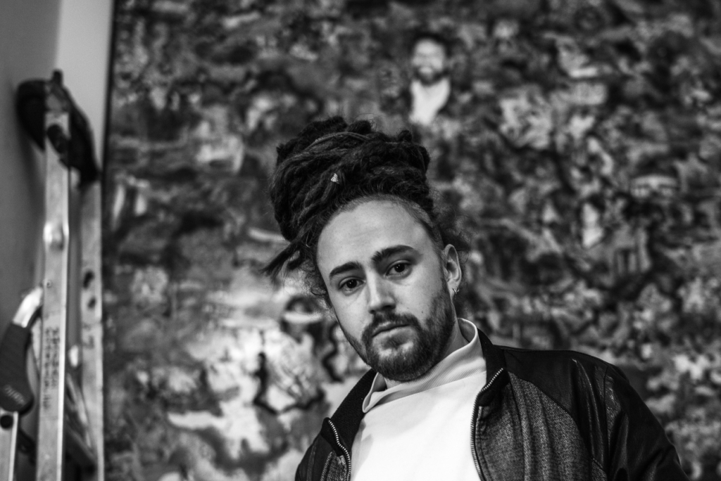 Mann mit Dreadlocks und Bart vor unscharfem Hintergrund, neben ihm eine Leiter.