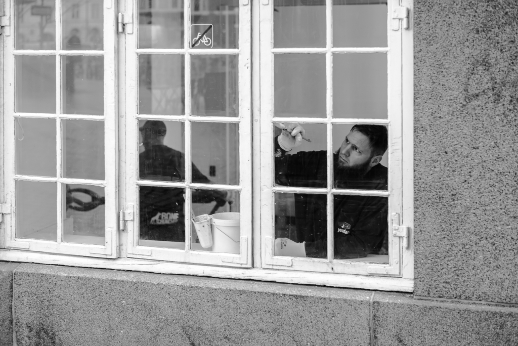 Person arbeitet konzentriert hinter einem Fenster, Werkzeuge und Fahrradverbotszeichen sichtbar.