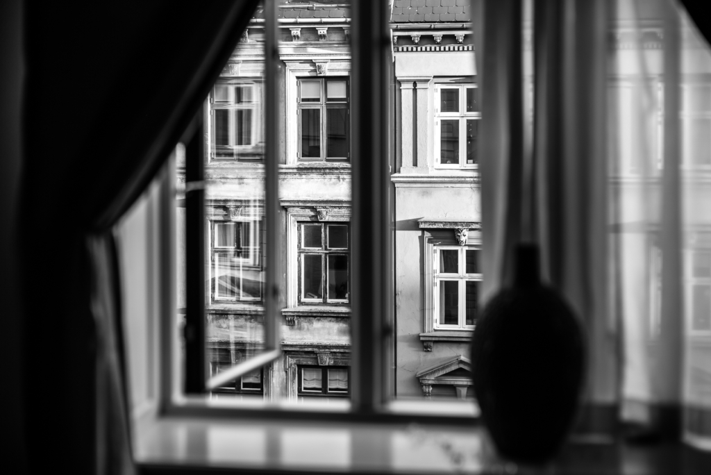 Alter Gebäudefassade durch Fensterscheibe mit Vase im Vordergrund in Schwarz-Weiß.