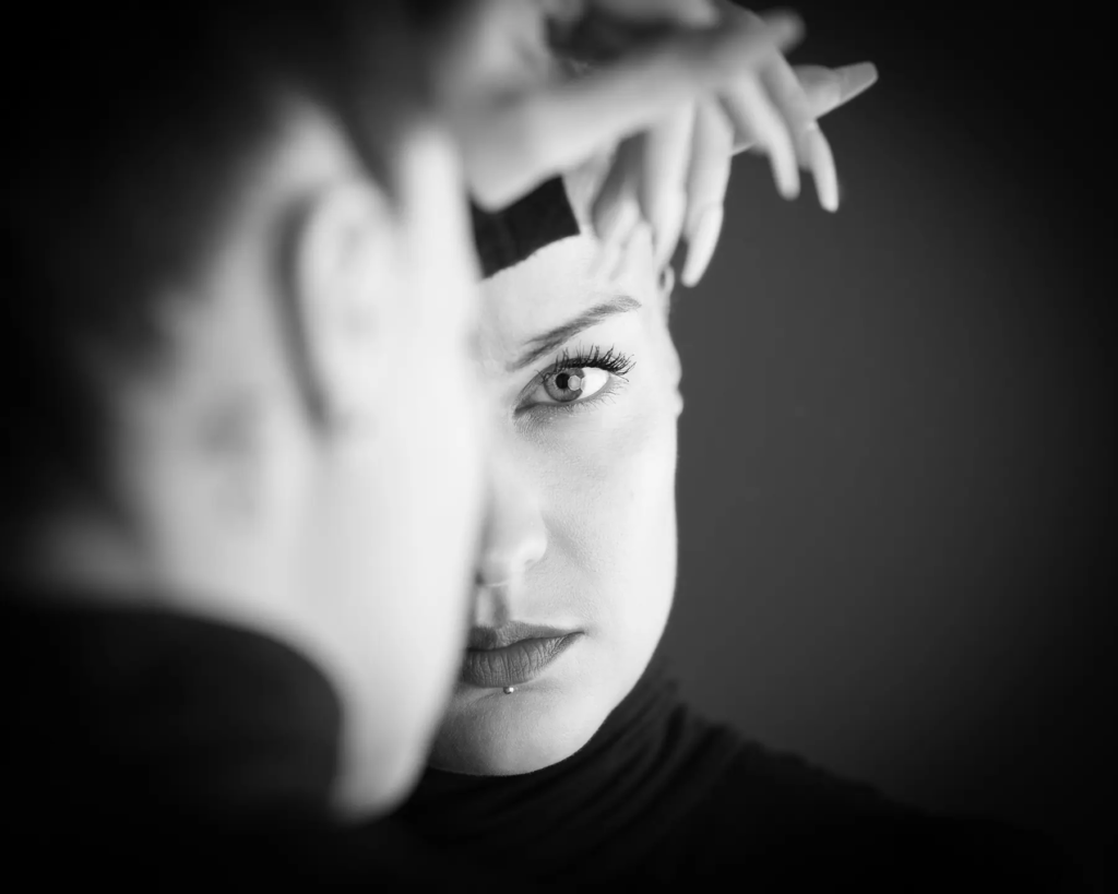 Schwarz-weiß Porträt einer Person, mit Gesicht teilweise von unscharfem Kopf verdeckt.