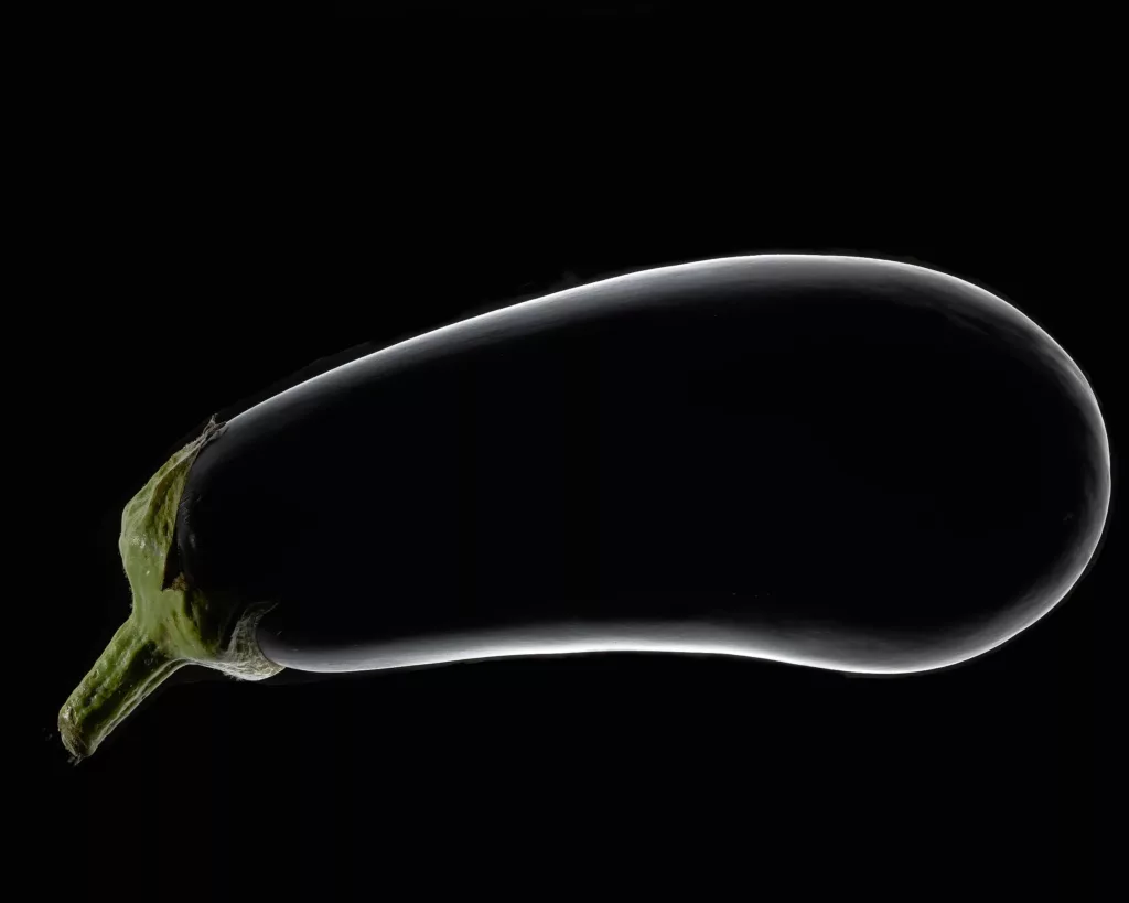 Dunkelviolette Aubergine vor schwarzem Hintergrund.