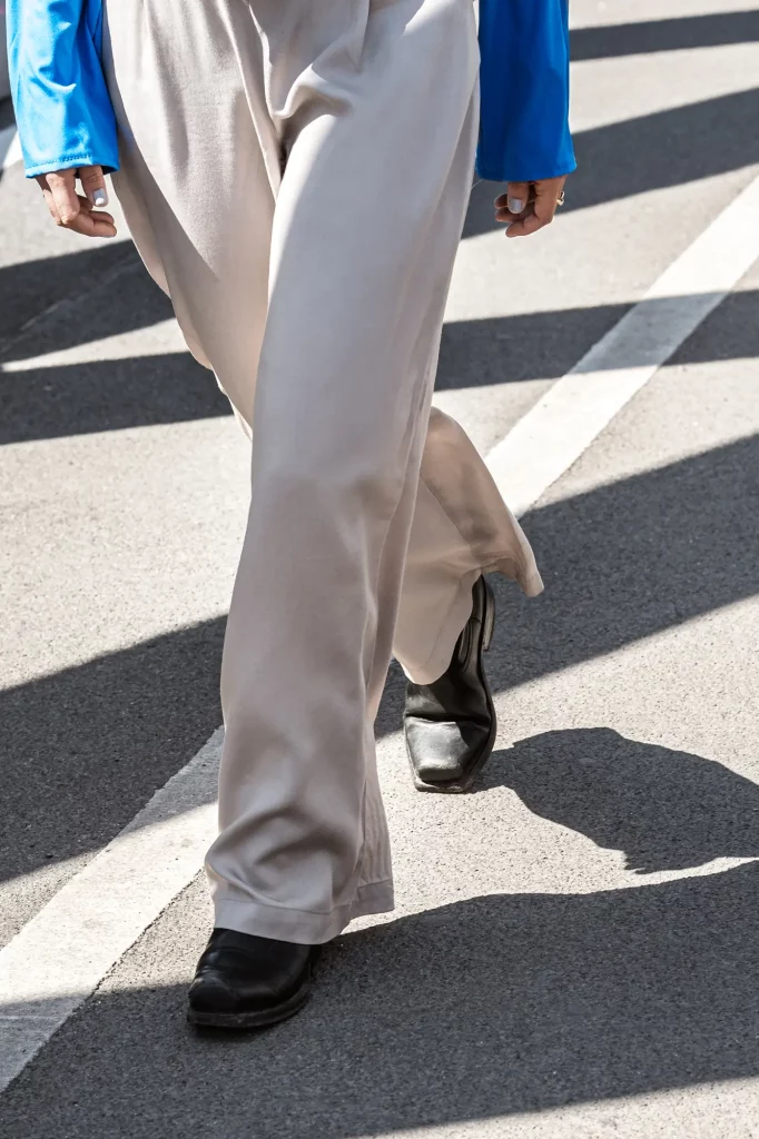 Person in blauer Jacke und cremefarbener Hose auf gepflasterter Straße, schwarze Schuhe.