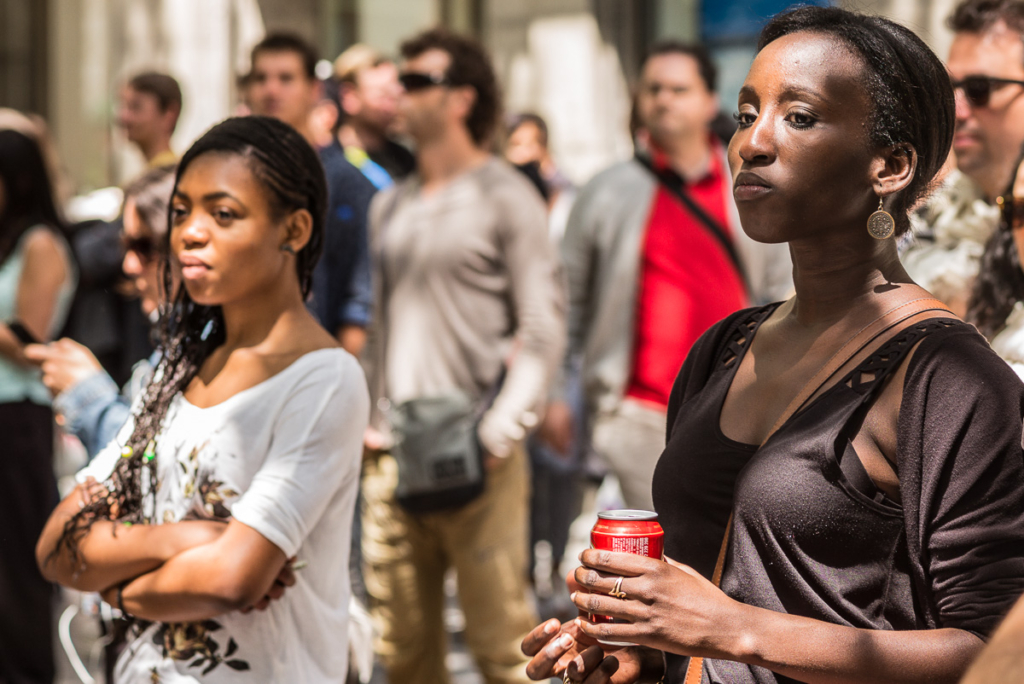 Gruppe von Menschen im Freien, zwei Frauen vorn, eine hält eine Getränkedose, tagsüber.