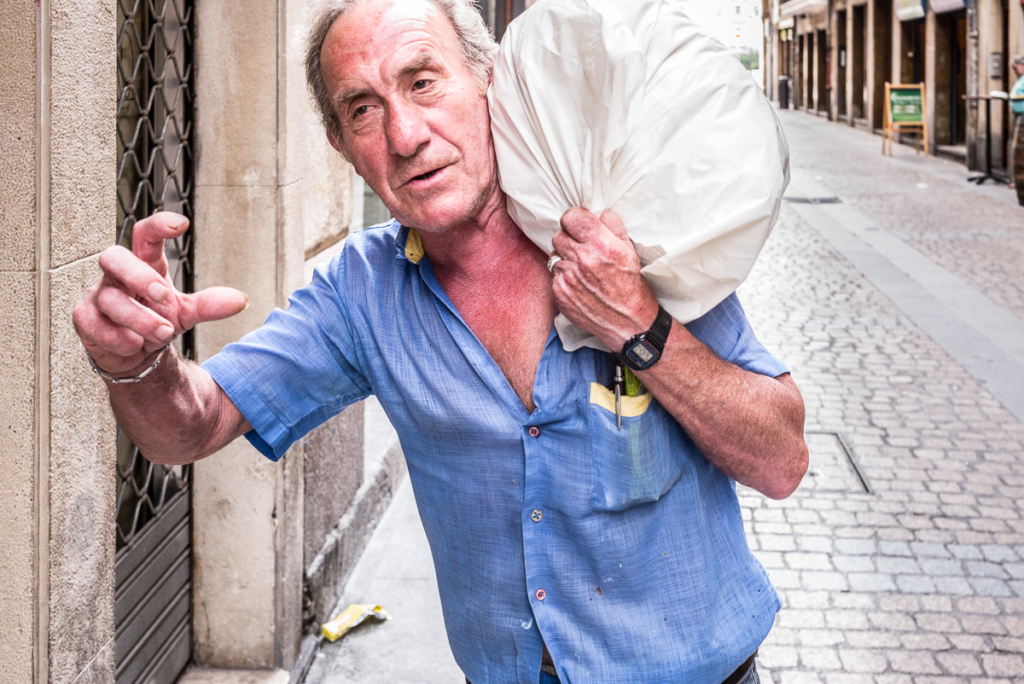 Mann in blauem Hemd trägt weißen Sack auf Schulter in städtischer gepflasterter Straße