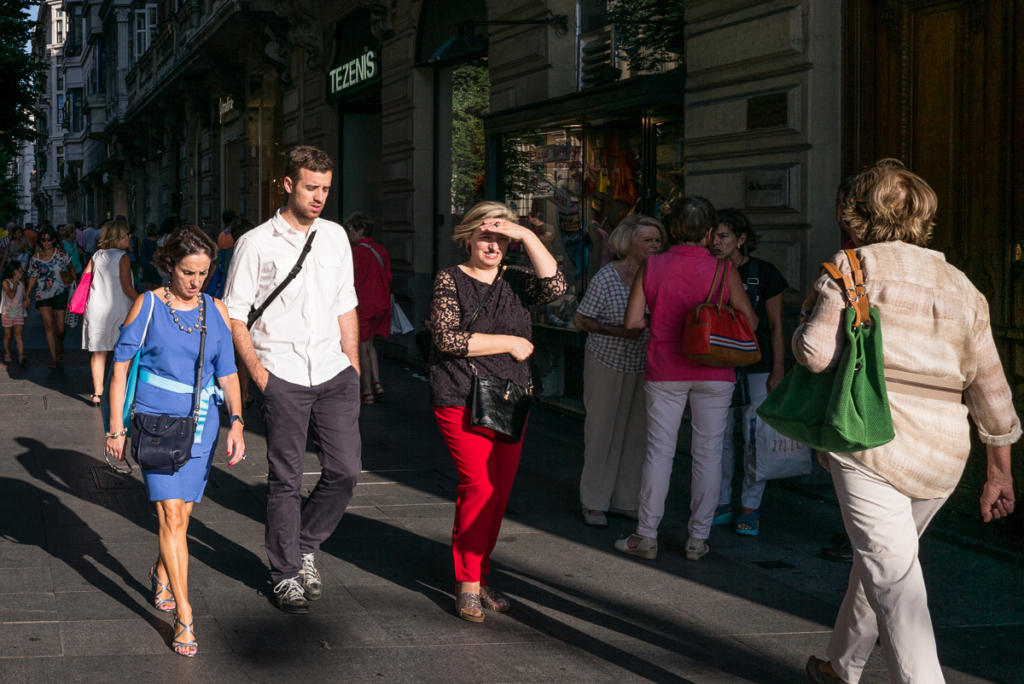 Belebter Bürgersteig in der Stadt, Geschäft mit "Tezenis"-Schild im Hintergrund sichtbar.