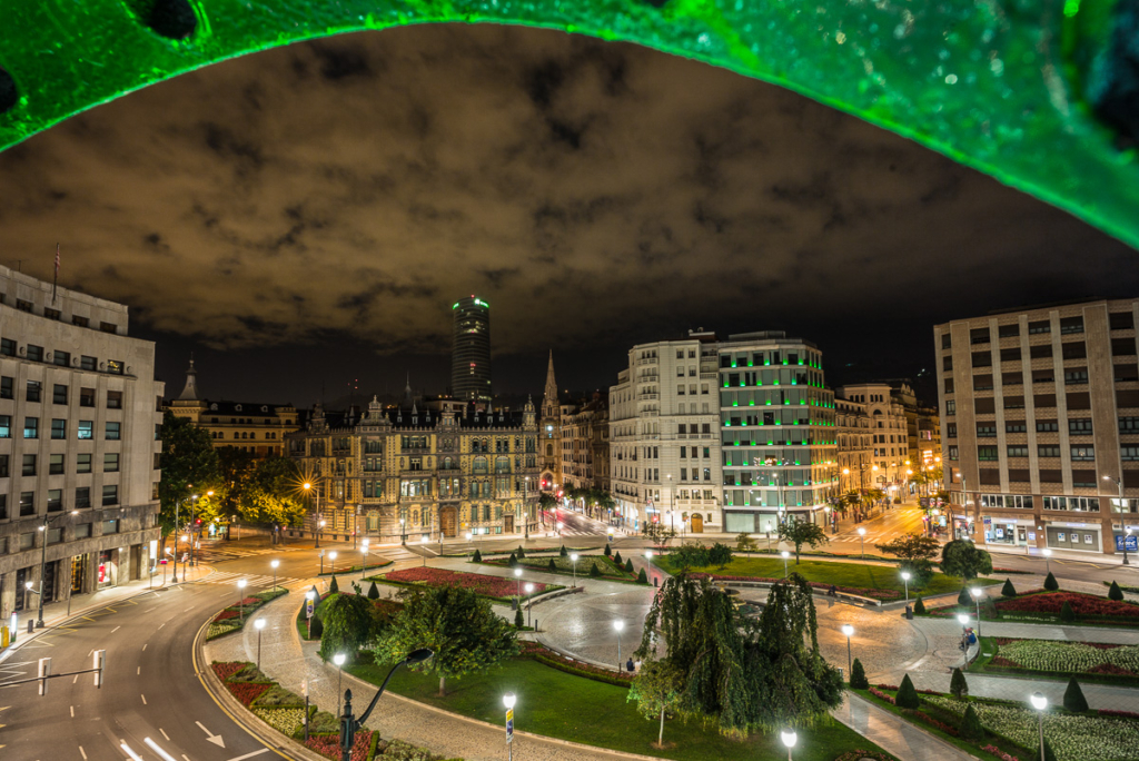 Nächtliche Stadtansicht mit beleuchtetem Platz, umgeben von historischen und modernen Gebäuden.
