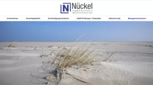 Ingenieurbüro Nückel, Sandlandschaft mit Gras und klarblauem Himmel, Navigationsleiste oben.