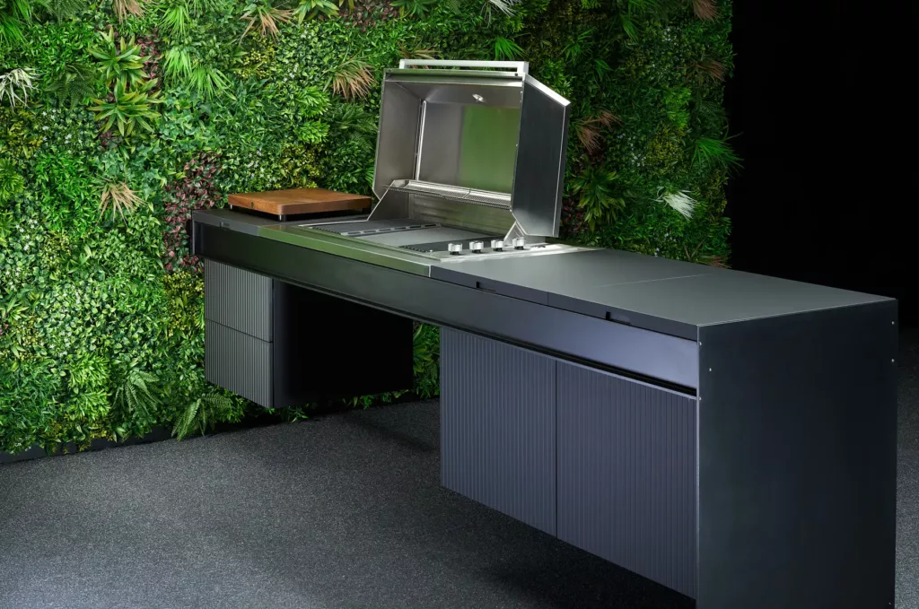 Moderner schwarzer Grill in stilvoller Outdoor-Küche vor üppiger grüner Pflanzenwand.