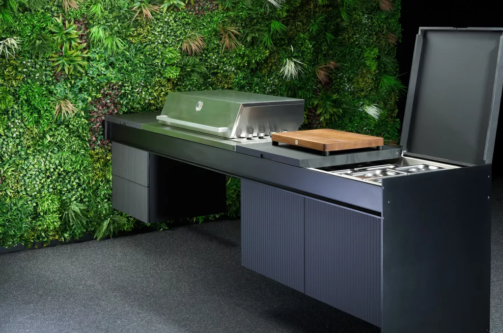 Moderner Außengrill mit Schneidebrett, Ablagefächern, Pflanzenwand im Hintergrund.