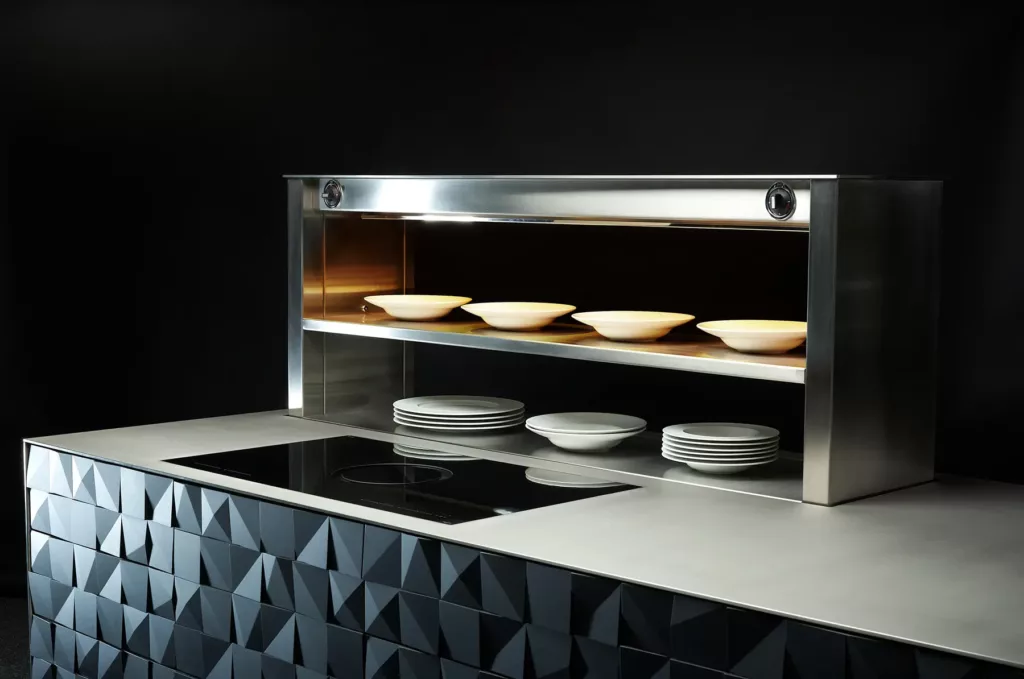 Moderne Küchentheke mit geometrischer Front, Kochfeld und Edelstahlregal mit weißen Tellern