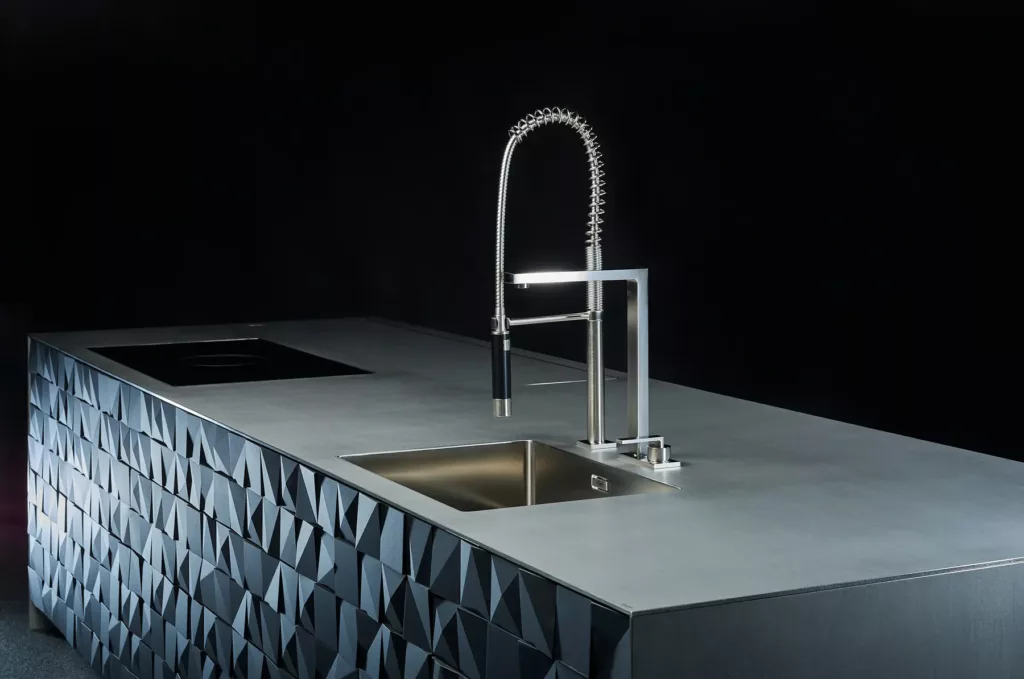 Moderner Küchenblock mit geometrischer Oberfläche, Spüle und schicker Armatur.