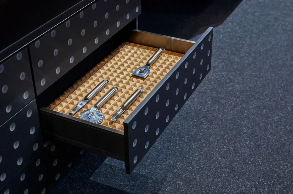 Schublade mit Punkten, enthält Küchenutensilien mit Metallgriffen auf rutschfester Unterlage.