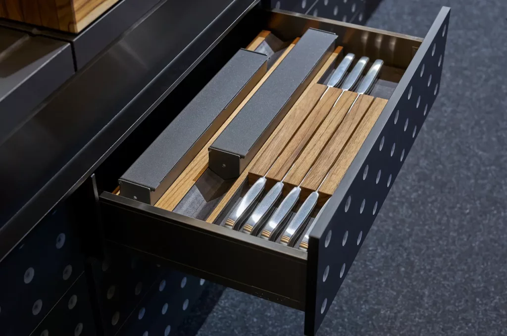 Geöffnete Küchenschublade mit Holzgriffmessern, schwarze Front mit weißen Punkten.