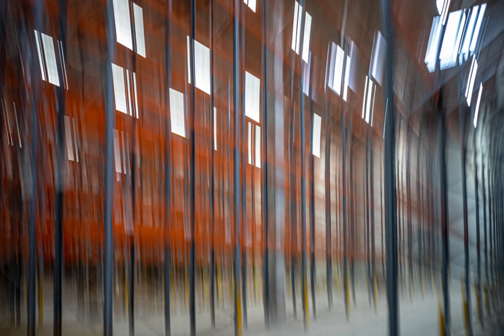 Abstraktes Lagerhausbild mit unscharfen Säulen, orangefarbener Struktur und Lichtreflexionen.