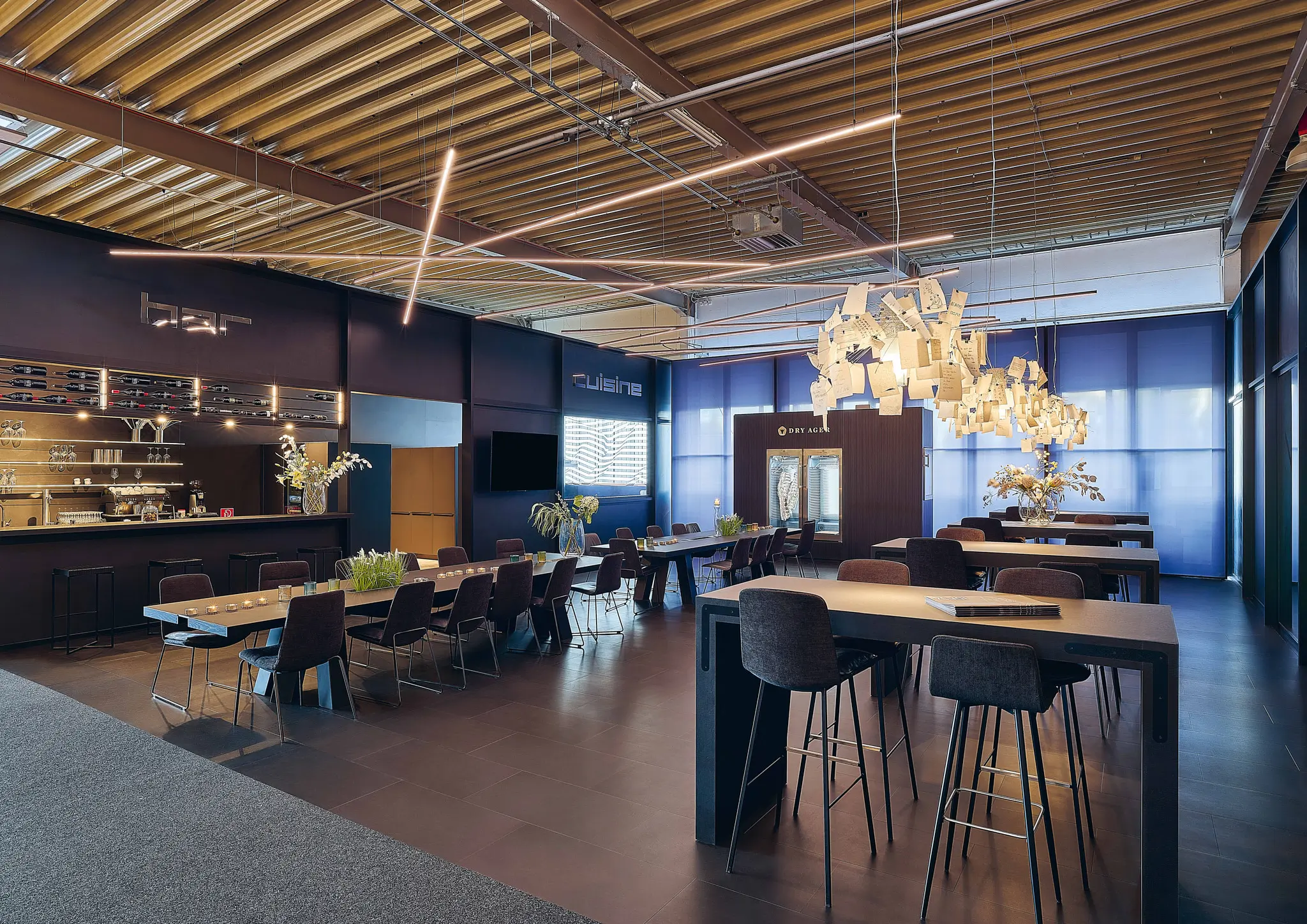 Moderner Essbereich mit langer Tafel, Bar im Hintergrund, modernen Lampen und Blumendekoration.