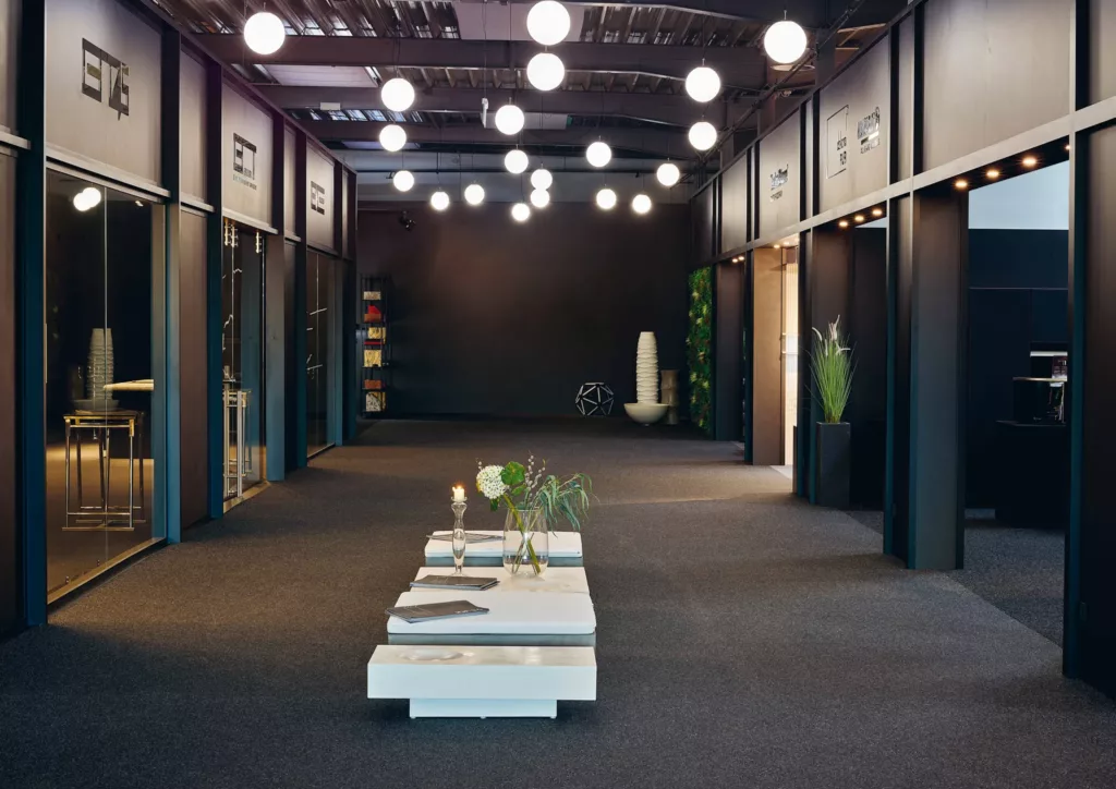 Moderner Ausstellungsraum mit Blumen auf zentralem Tisch, dunklen Wänden und stimmungsvoller Beleuchtung.