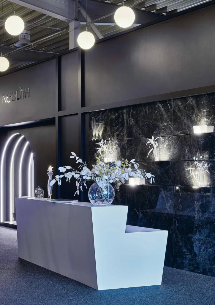 Moderner Empfangsbereich mit weißem Tresen, Vase und schwarzer Marmorwand mit Neolith-Logo.