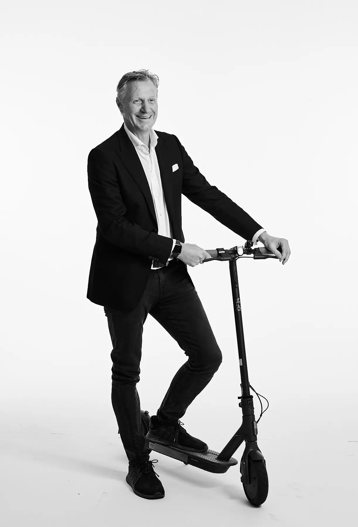 Mann in formeller Kleidung steht auf Elektroroller vor neutralem Hintergrund.