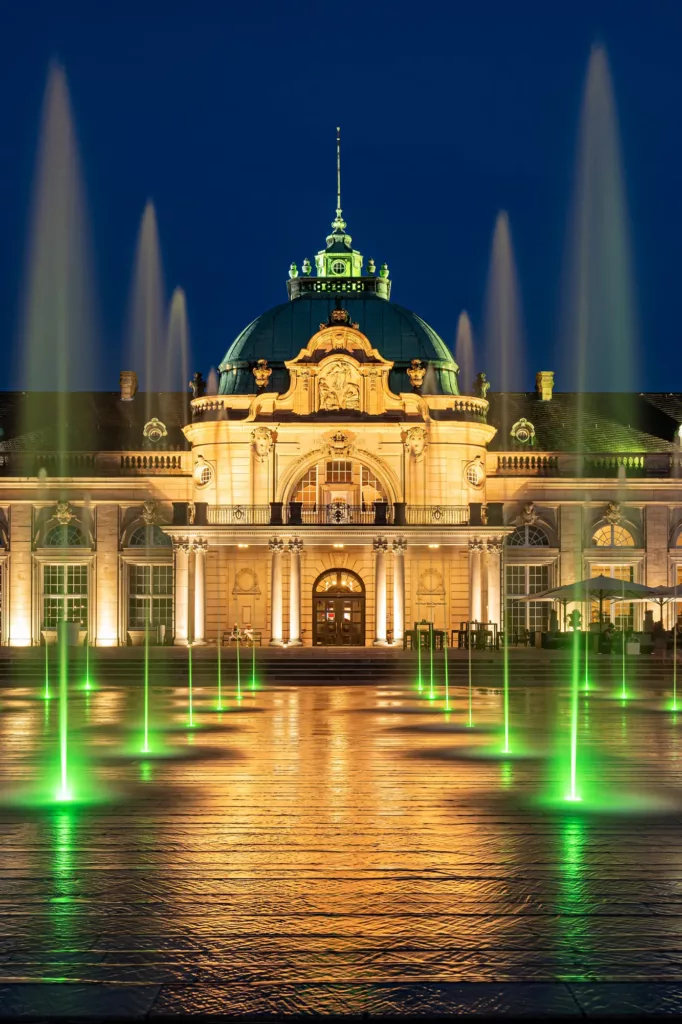 Historisches Gebäude bei Nacht mit Kuppel und grün beleuchteten Wasserfontänen davor.