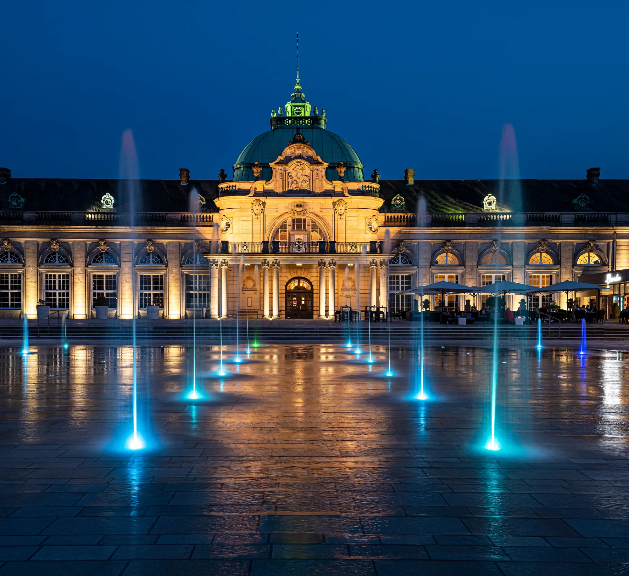 Historisches Gebäude bei Nacht, Kuppel, beleuchtete Springbrunnen auf gepflastertem Platz.