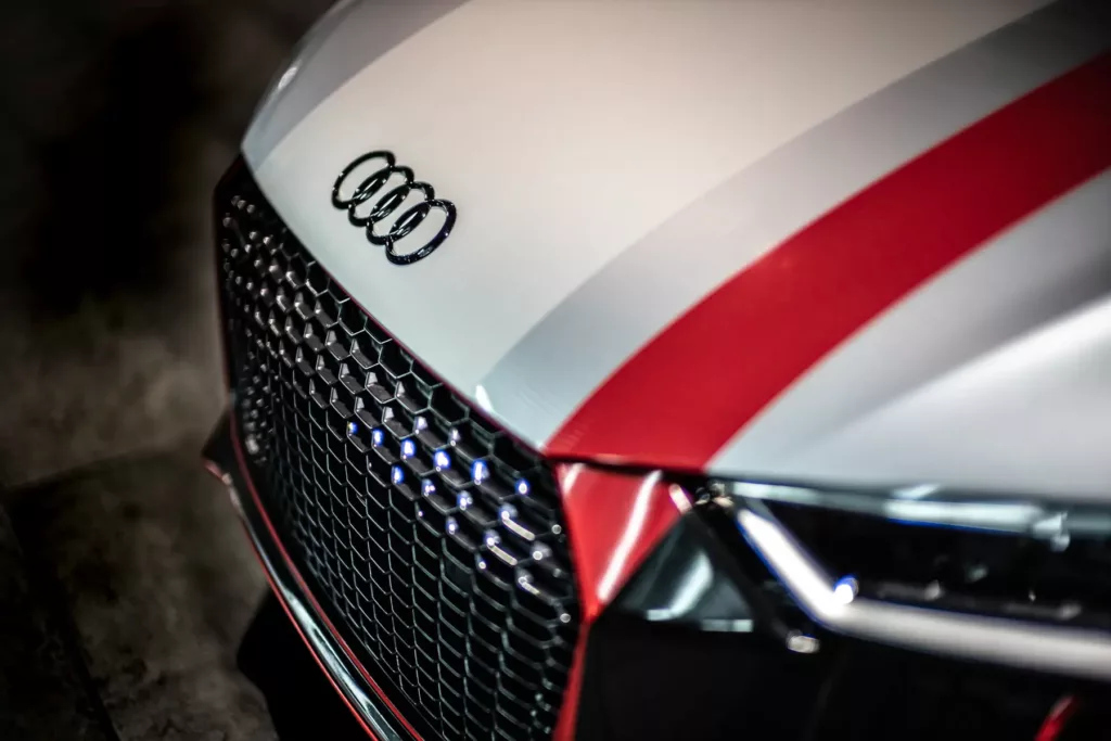 Audi-Frontgrill mit Logo und einer roten Linie über der weißen Motorhaube.
