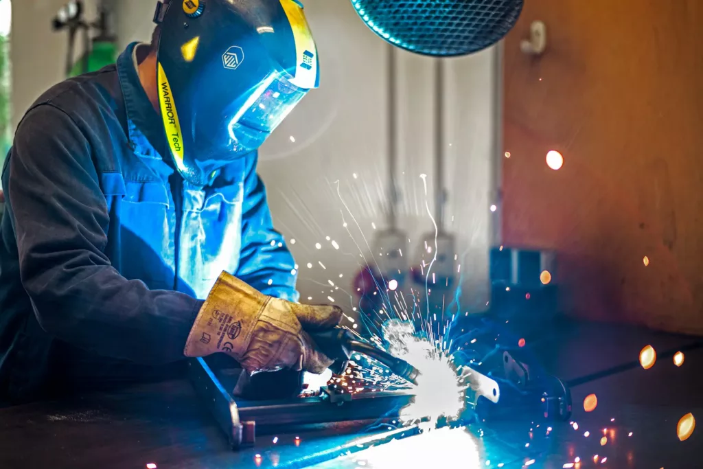Eine Person im Schutzanzug schweißt, mit Funkenflug von der Schweißstelle.