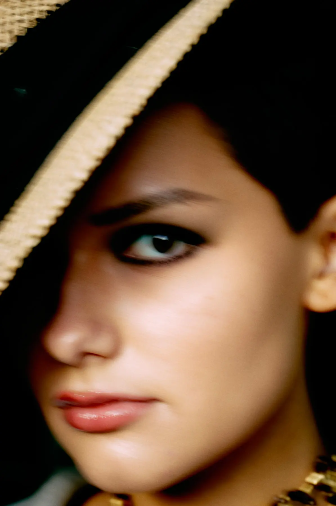 Nahaufnahme eines geschminkten Gesichts teils mit schwarzem Hut, Fokus auf Auge und Lippen.