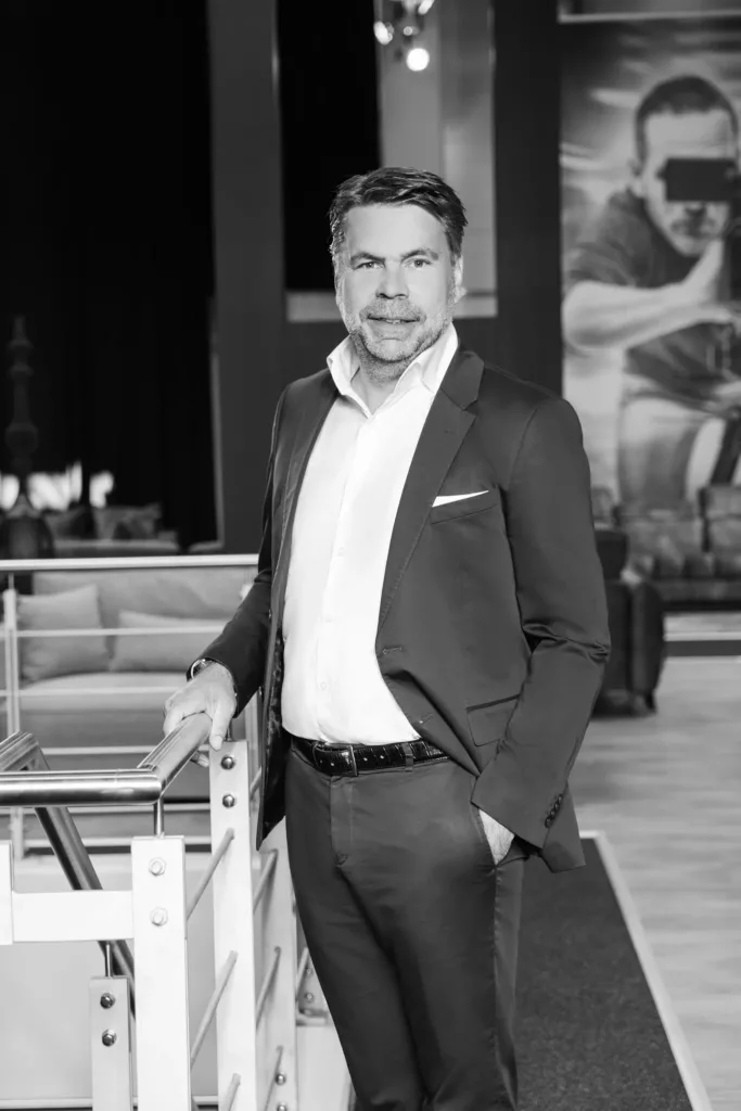 Mann in Anzug steht an Geländer vor Sofas und großem Bild, schwarz-weiß Fotografien.