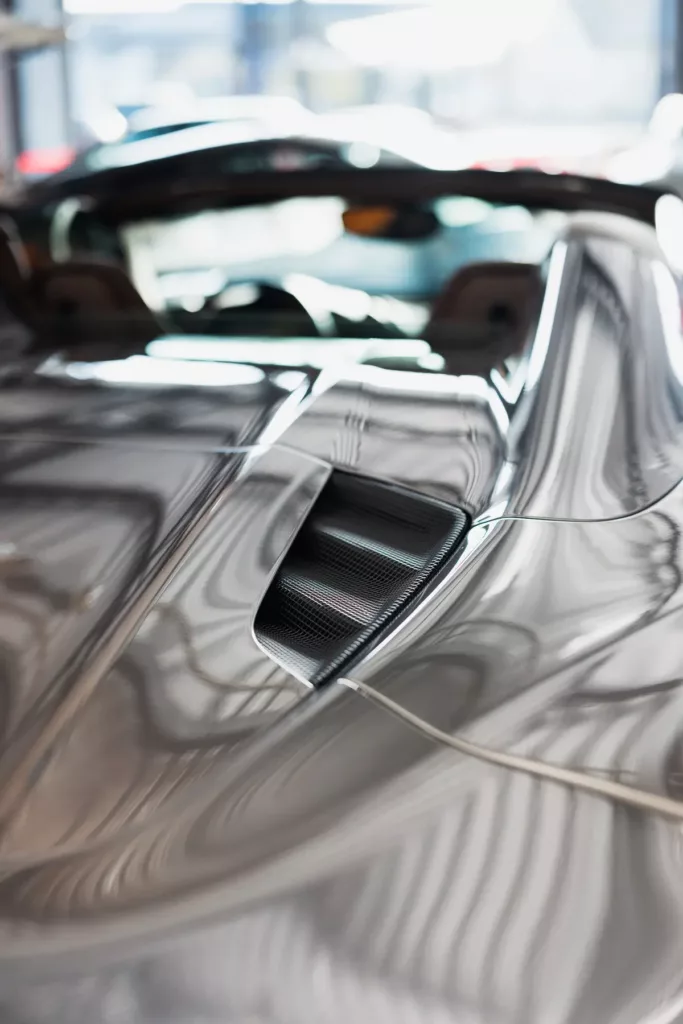 Glänzendes Autodach mit Belüftungsöffnung und Lichtreflexionen, unscharfer Innenraum im Hintergrund.