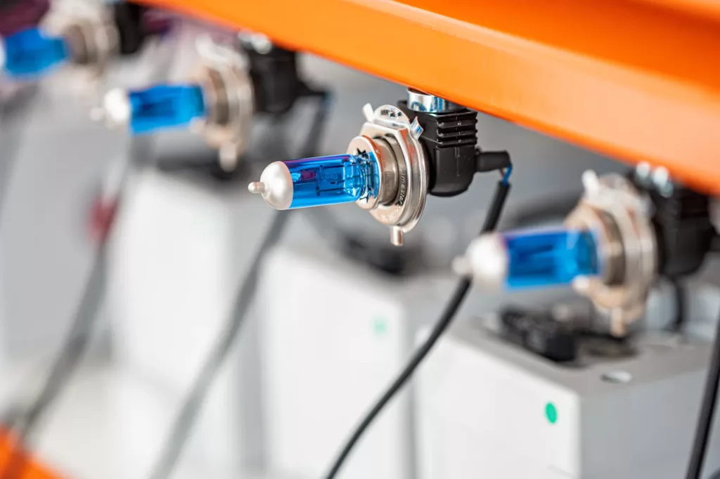 Blaue Halogenlampen an oranger Leiste mit elektrischen Anschlüssen, linear angeordnet.