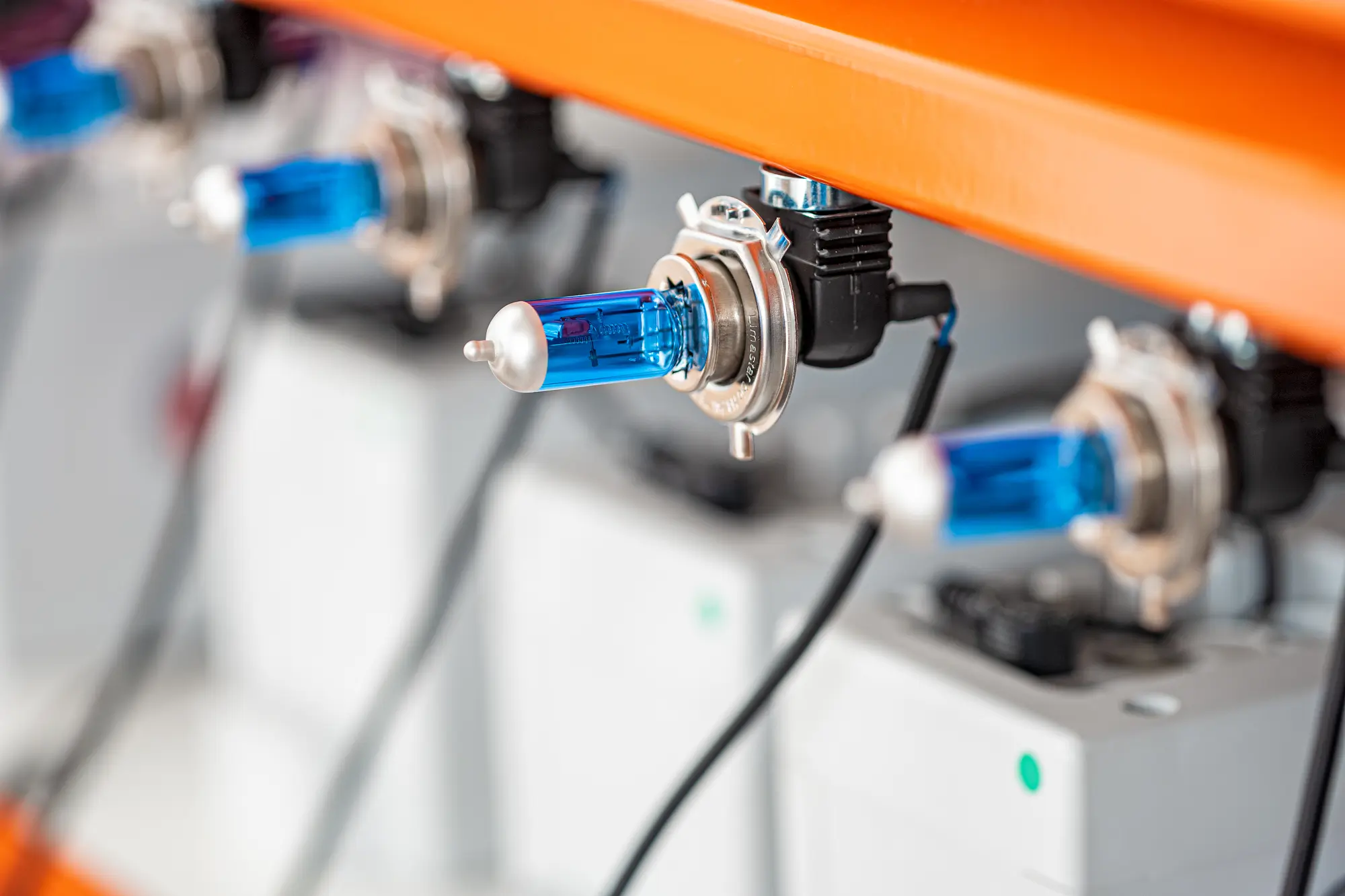 Blaue Halogenlampen an oranger Leiste mit elektrischen Anschlüssen, linear angeordnet.