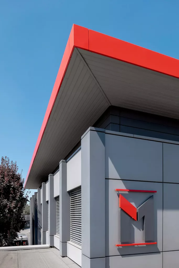 Modernes Gebäude mit grauen Fassaden, roten Dachakzenten und einem roten, grauen Logo an der Wand.