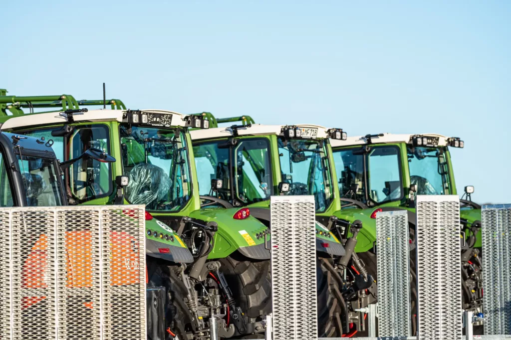 Grüne Traktoren mit geschlossenen Kabinen hinter metallischen Gittern bei Tageslicht.