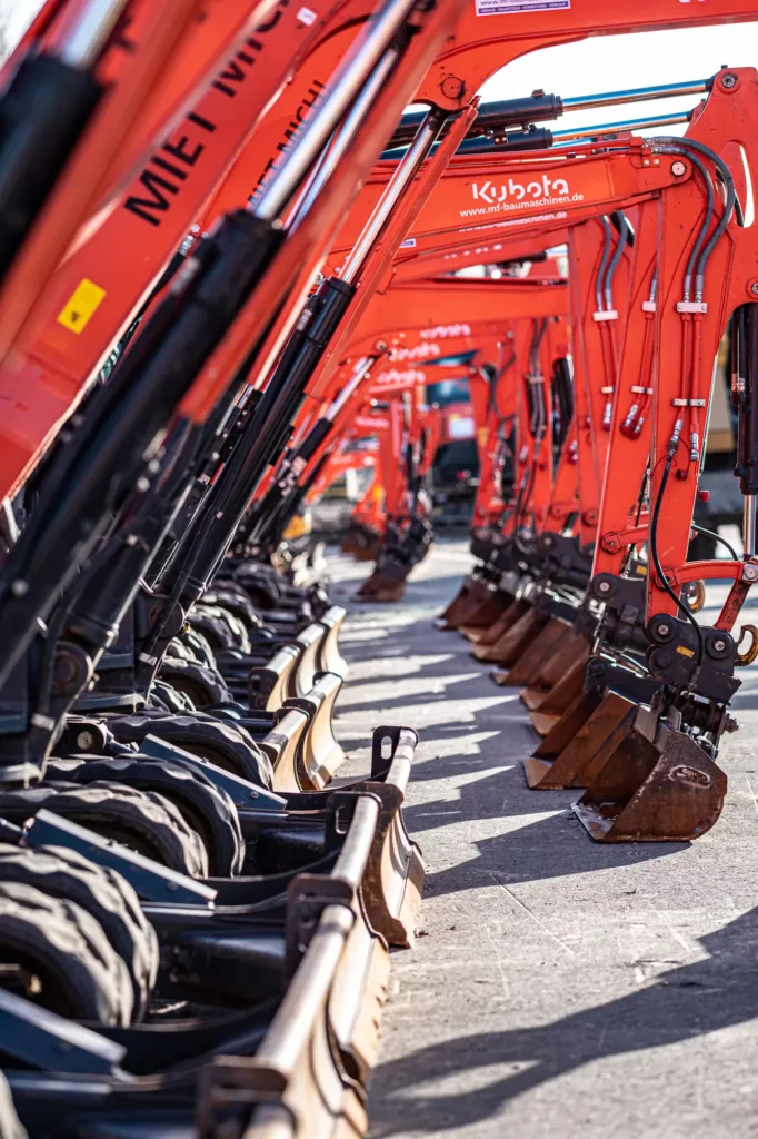 Orangefarbene Baggerarme mit Schaufeln und Mietinformationen in einer Reihe aufgestellt.