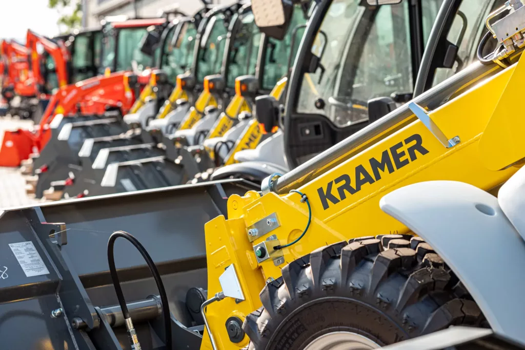 Gelbe Kramer-Fahrzeuge, vermutlich Bagger oder Radlader, in einer geordneten Reihe aufgestellt.