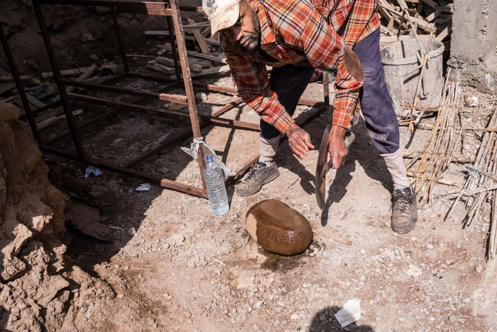 Mann bearbeitet großen Stein mit Werkzeug, Trinkflasche daneben, staubige Baustelle.