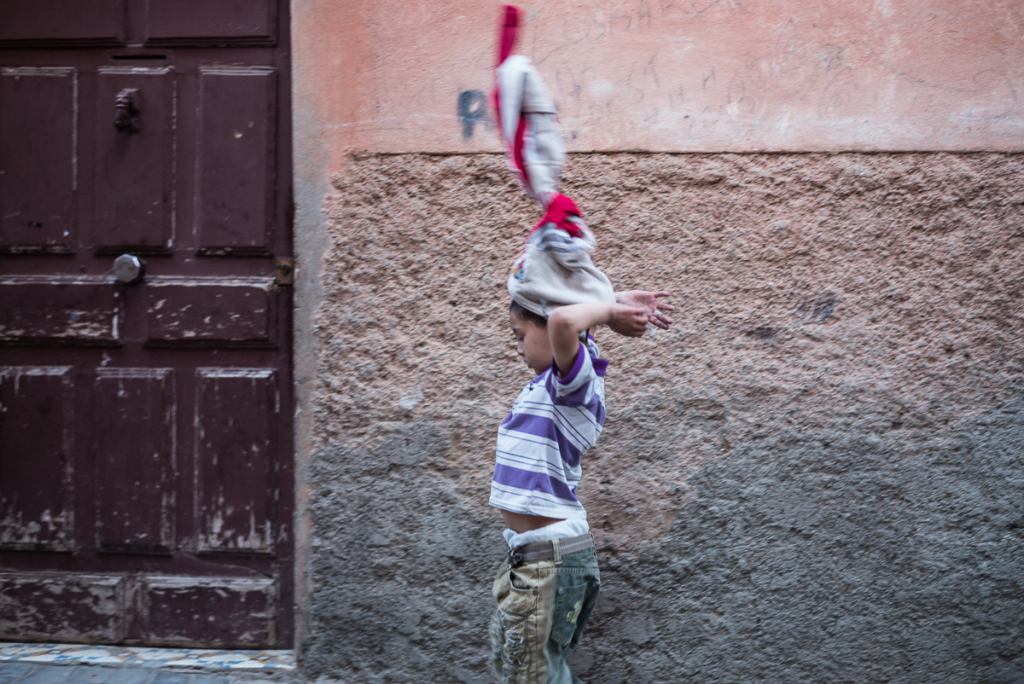 Kind läuft mit verschränkten Händen auf Straße, Hintergrund bunte Wand, Holzstür.
