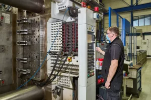 Industriemaschine mit Bedienfeld, Person mit Maske arbeitet in einer Fabrikumgebung.