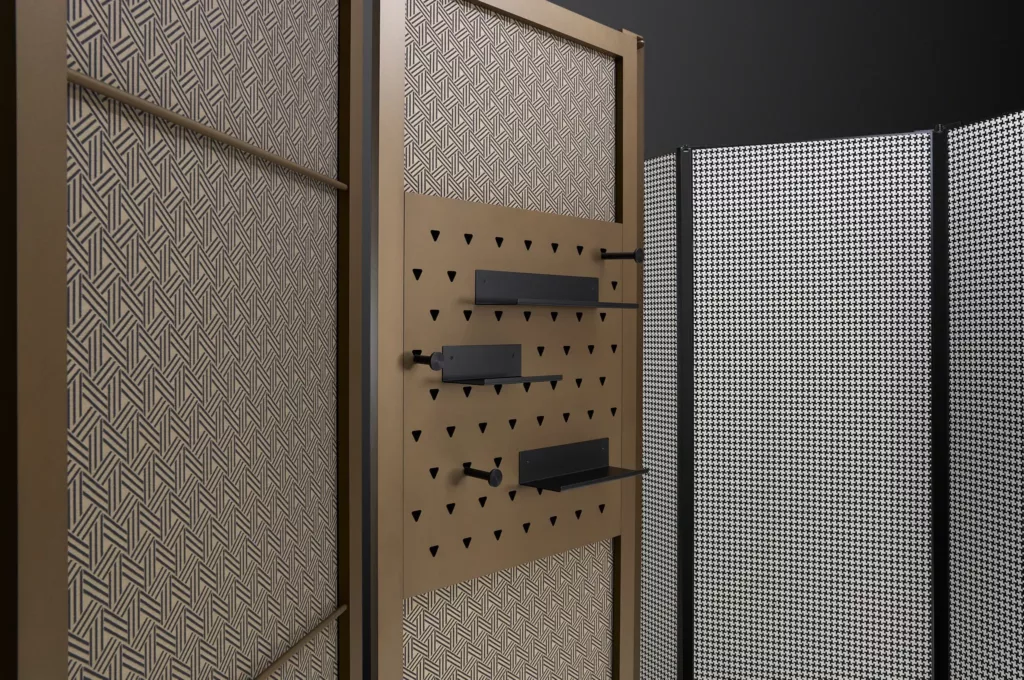 Raumteiler mit geometrischem Muster und verstellbaren schwarzen Regalen auf perforierten Paneelen.