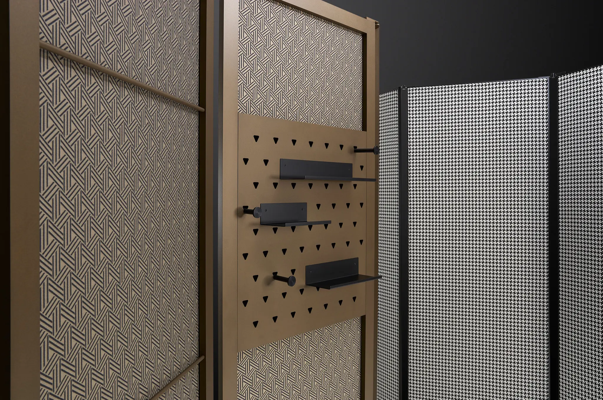 Raumteiler mit geometrischem Muster und verstellbaren schwarzen Regalen auf perforierten Paneelen.