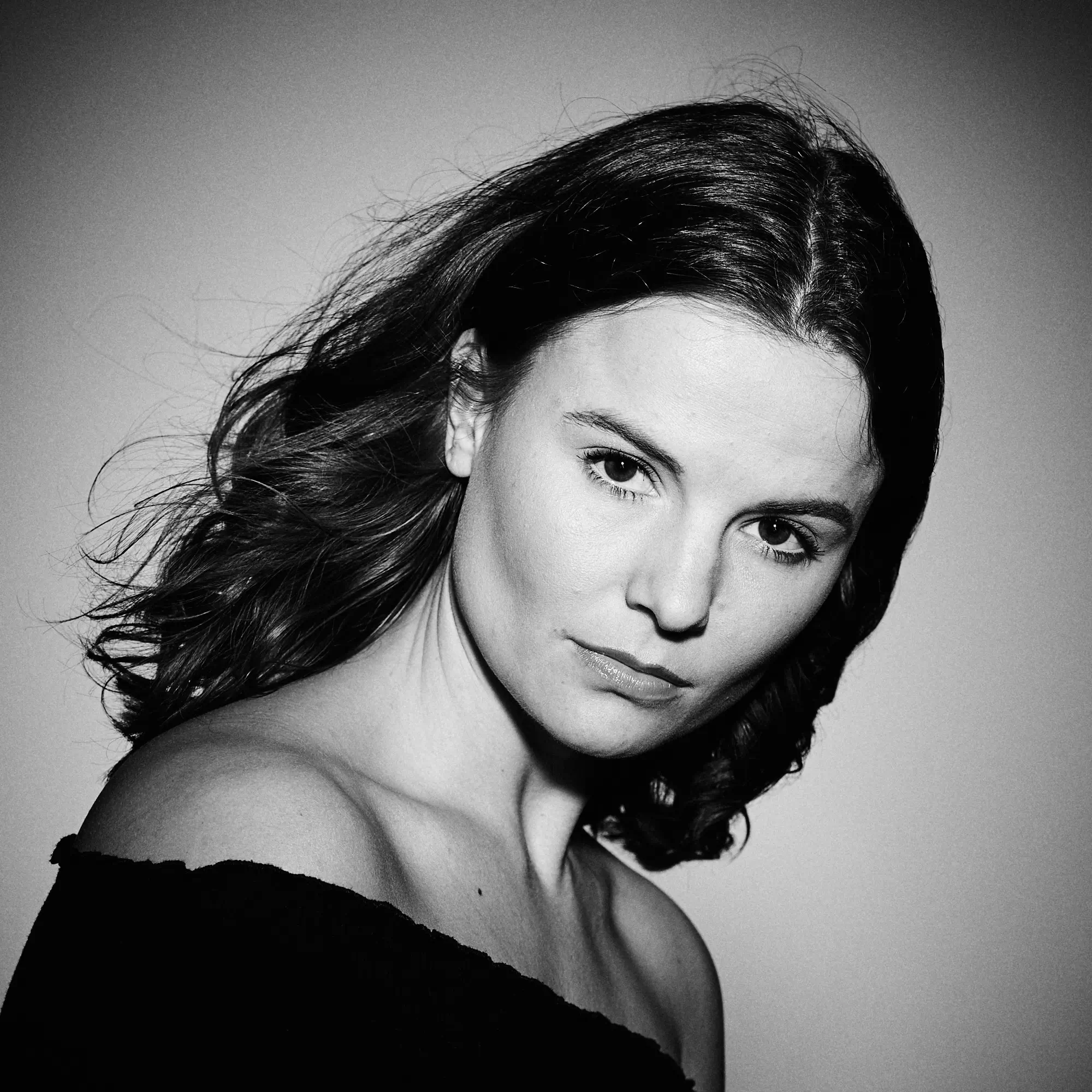 Frau mit offenen Haaren und schulterfreiem Oberteil in ernstem Schwarz-Weiß-Porträt.