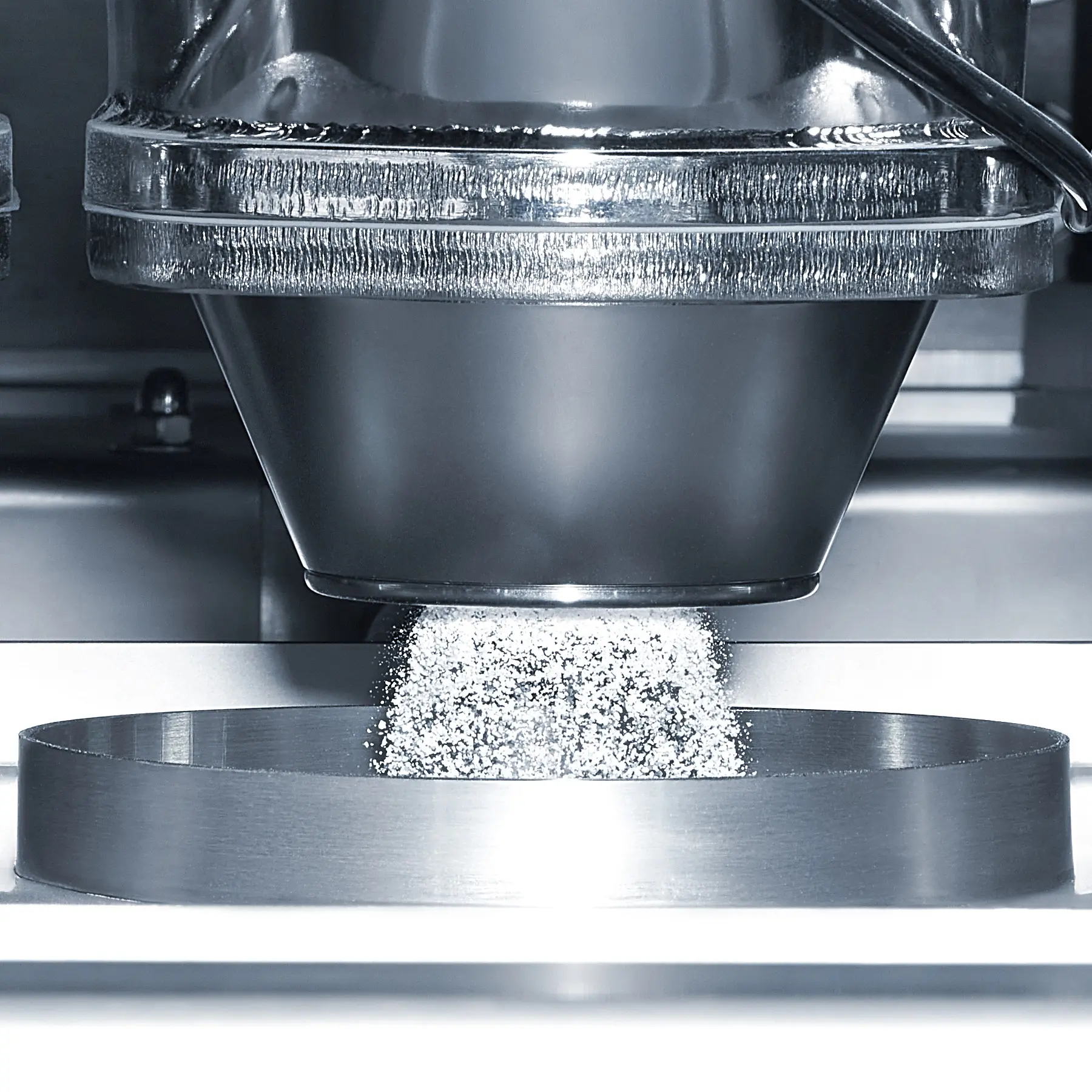 Industrieller Prozess mit Pulver, das in einen runden Behälter fällt, umgeben von Metallumgebung.