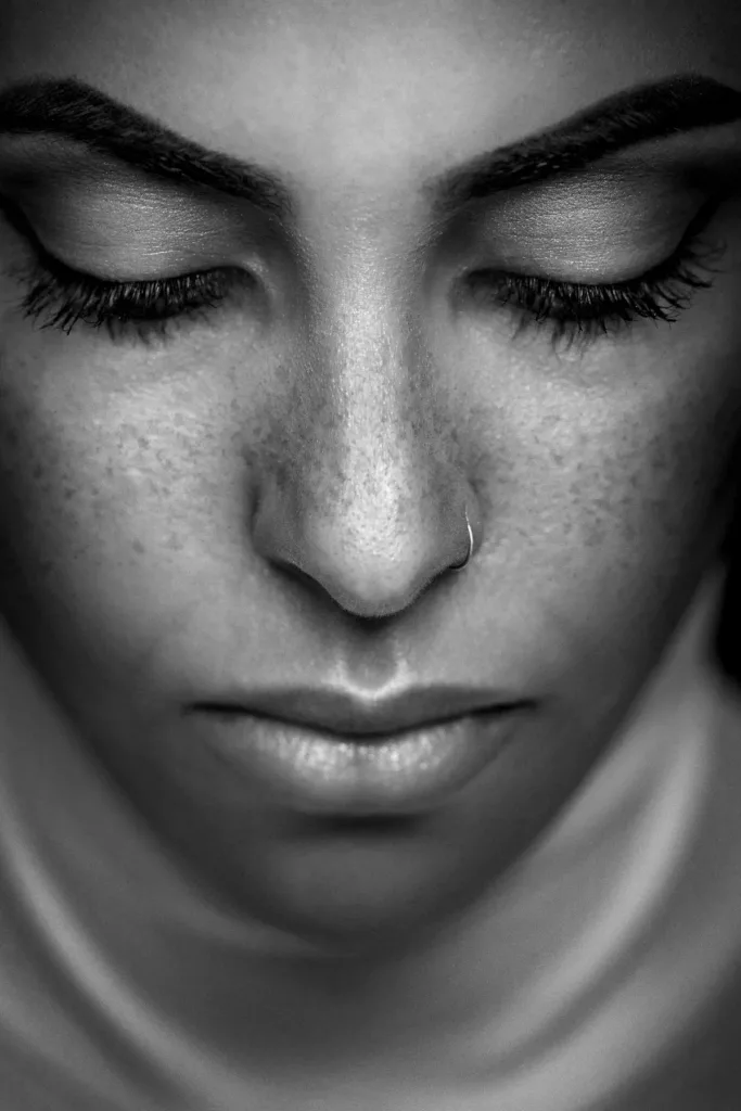 Schwarzweißportrait mit geschlossenen Augen, Nasenring und Sommersprossen sichtbar.