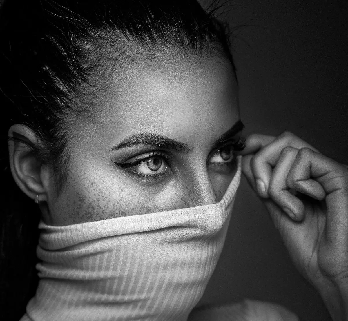 Frau zieht Rollkragenpullover über Mund, schwarz-weiß Fotografie, Augen und Sommersprossen sichtbar.