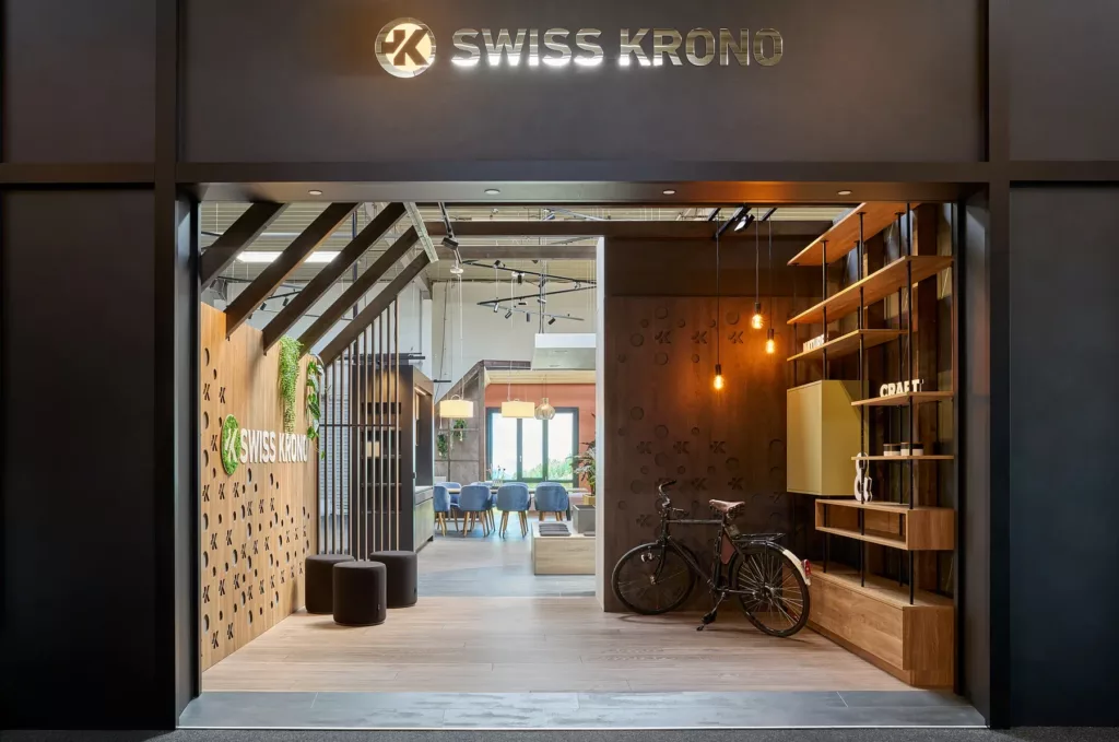 Moderner Swiss Krono Ausstellungsraum mit hölzernen Akzenten, Lampen, Fahrrad, Sitzbereich.