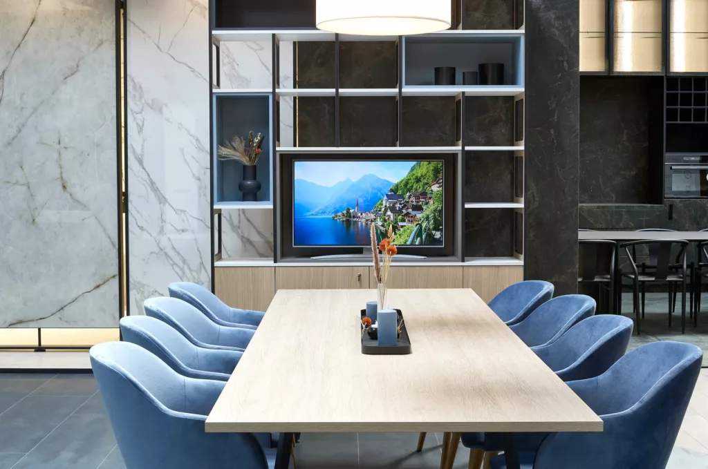Moderner Besprechungsraum mit Holztisch, blauen Stühlen, Marmorwand und Fernseher.