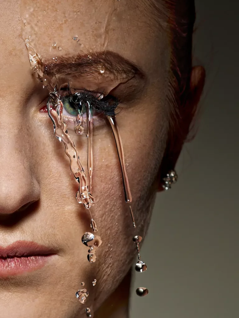Nahaufnahme eines Gesichts mit fließendem Wasser über dem linken Auge und feuchten Wimpern.