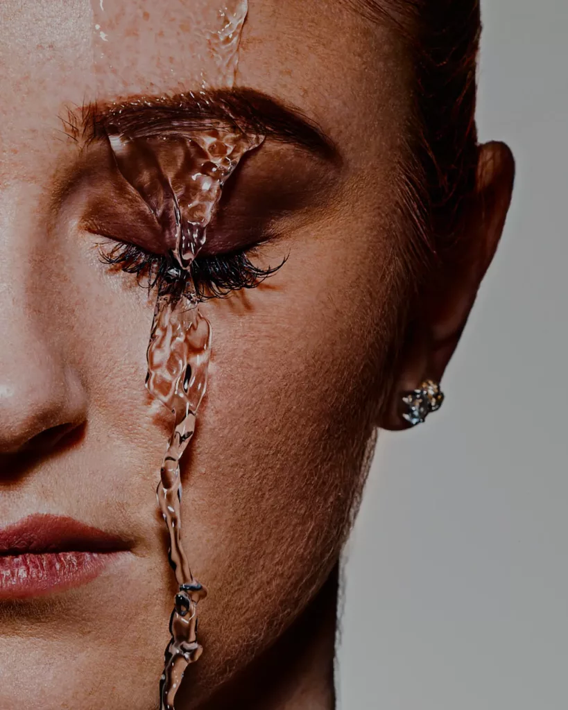 Nahaufnahme eines Gesichts mit Wasser auf Haut und geschlossenen Augen, Person trägt Ohrringe.