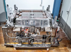 Industrielle Metallform mit Hydraulikanbindungen auf Holzboden in Werkstattumgebung.