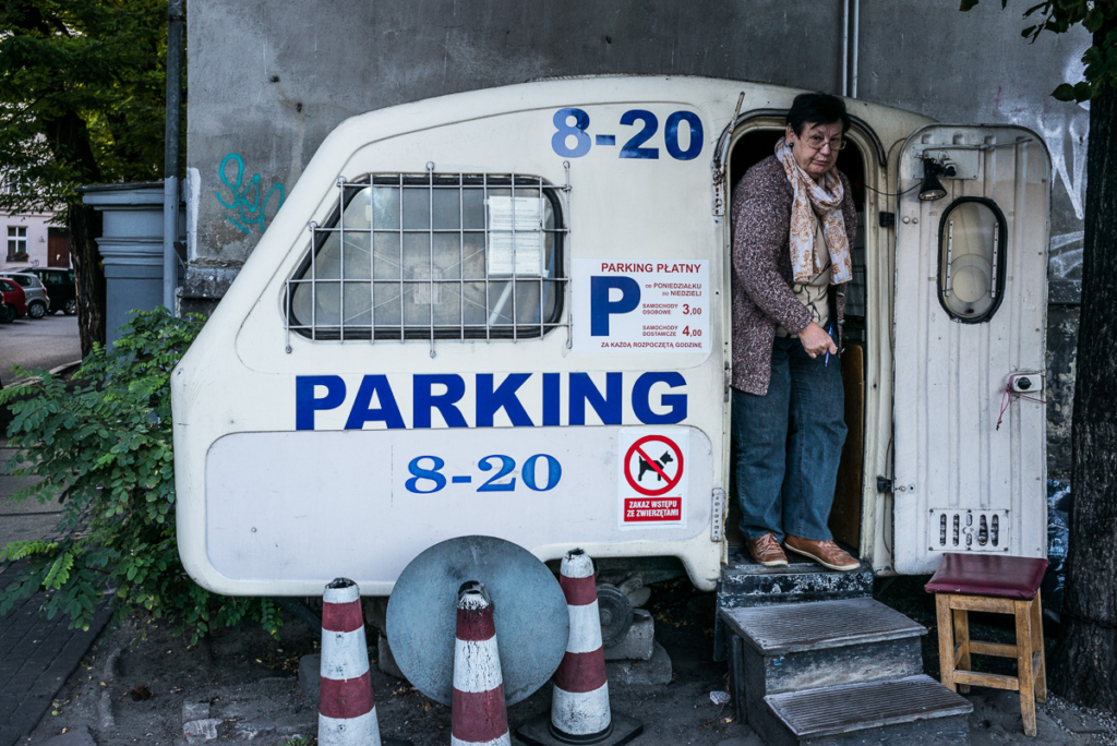 Kleiner Anhänger als Wachhäuschen auf Parkplatz, 8-20 Uhr, Person, Schilder und Absperrkegel.